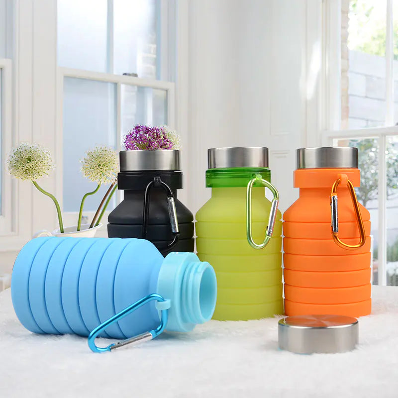 Colorful collapsible silicone water bottles in blue, orange, black, and green displayed on a table near a window