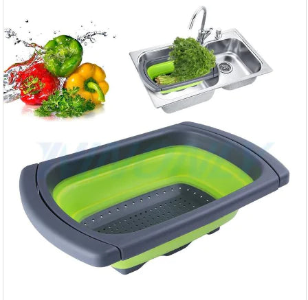 Green collapsible colander filled with fresh vegetables beside tomatoes and bell peppers