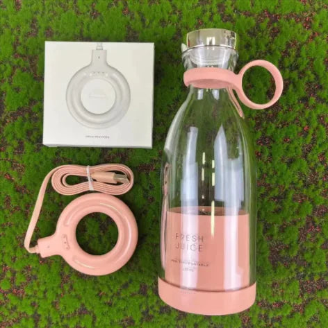 Pink Fixxora mini juice blender 350ml with magnetic charging cable and accessories on grass background.